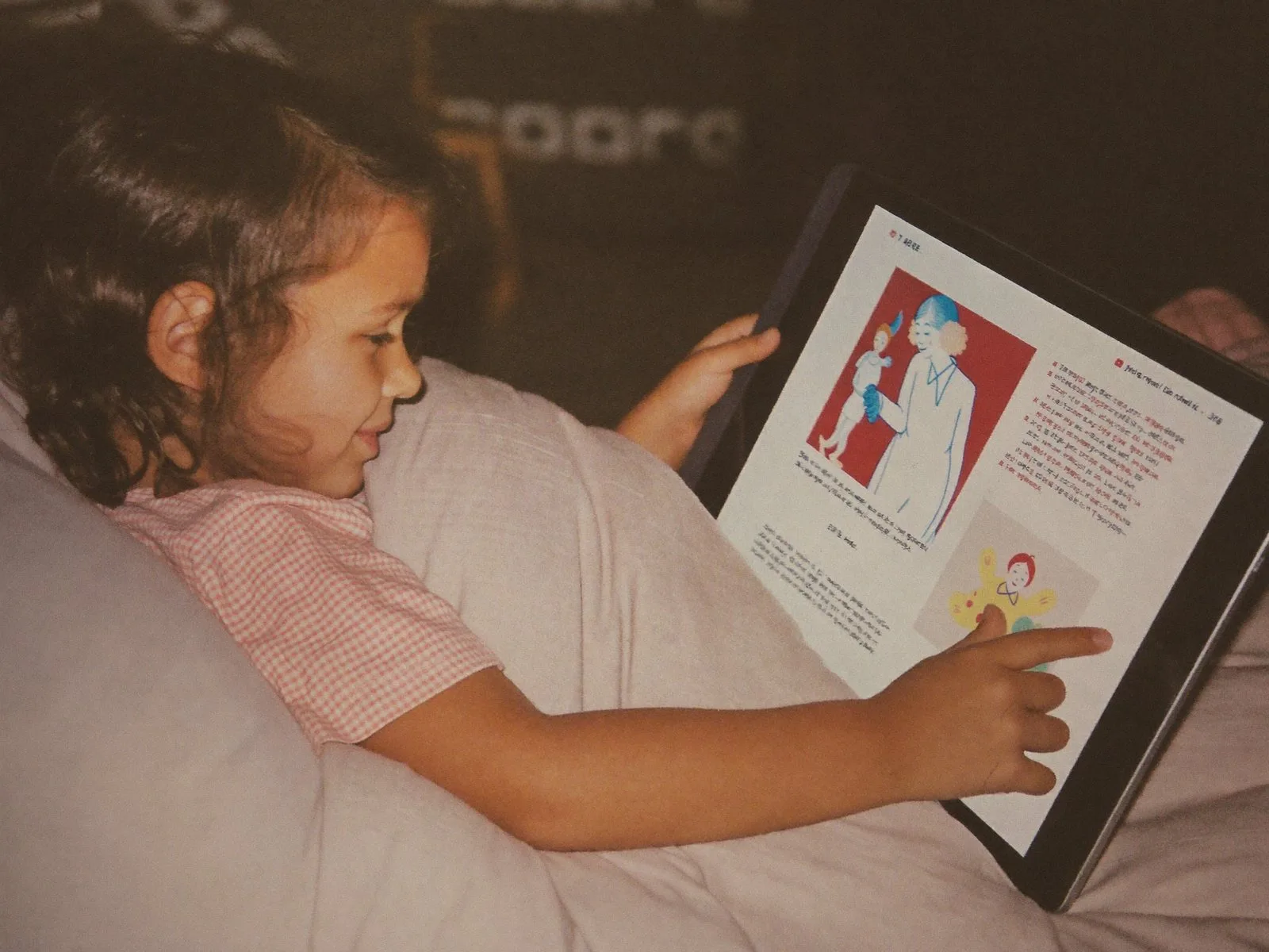 A child in bed listening to a phone propped on a picture book
